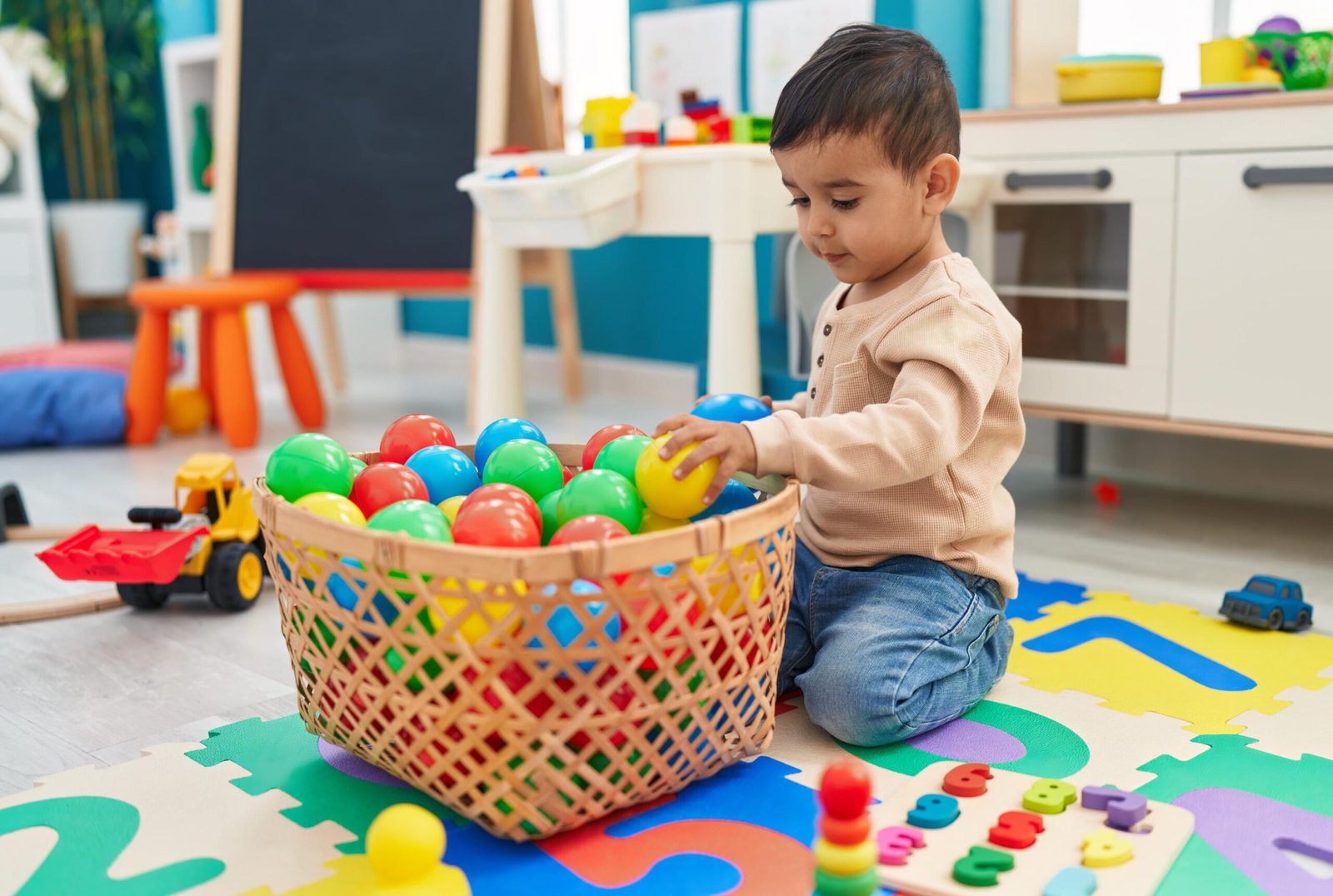 adorable-hispanic-toddler-playing-with-balls-sitting-floor-kindergarten-min