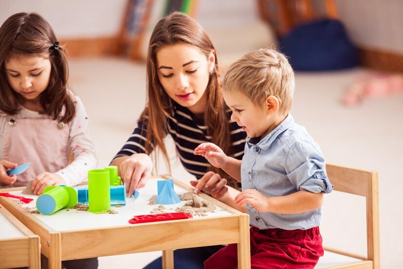 A therapist at Interactive Minds in Bahrain guides a young boy and girl as they engage in sensory play with kinetic sand.
