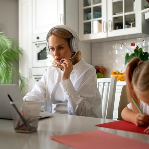 Parent Support for Work-Life Balance in Bahrain A mother works from home on her laptop while her young daughter colors beside her, illustrating the need for parent support resources from Interactive Minds.