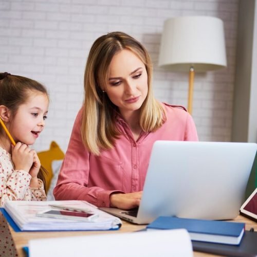 Parent Helping Child with Homework in Bahrain A mother in Bahrain helps her young daughter with homework on a laptop, using academic support resources from Interactive Minds.